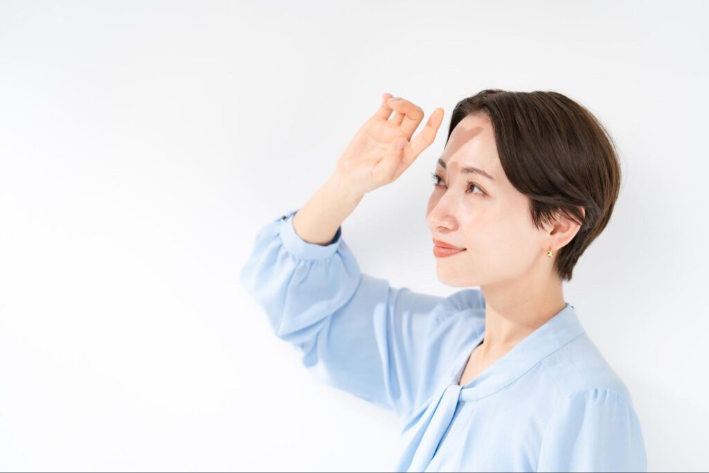 顔に手をかざして日光を遮っている女性