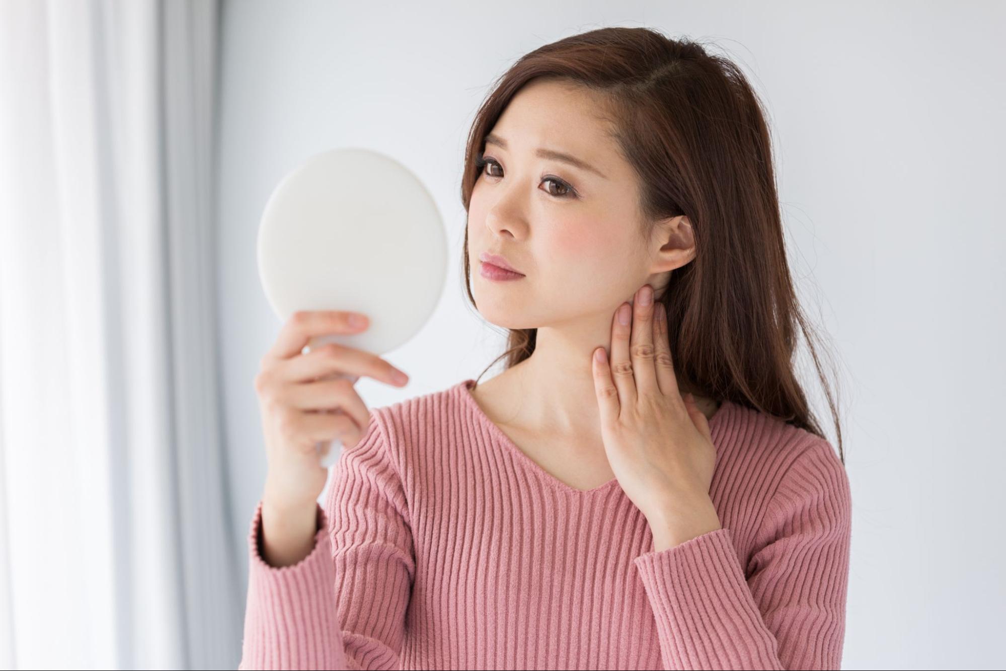 鏡を見てたるみを気にしている女性