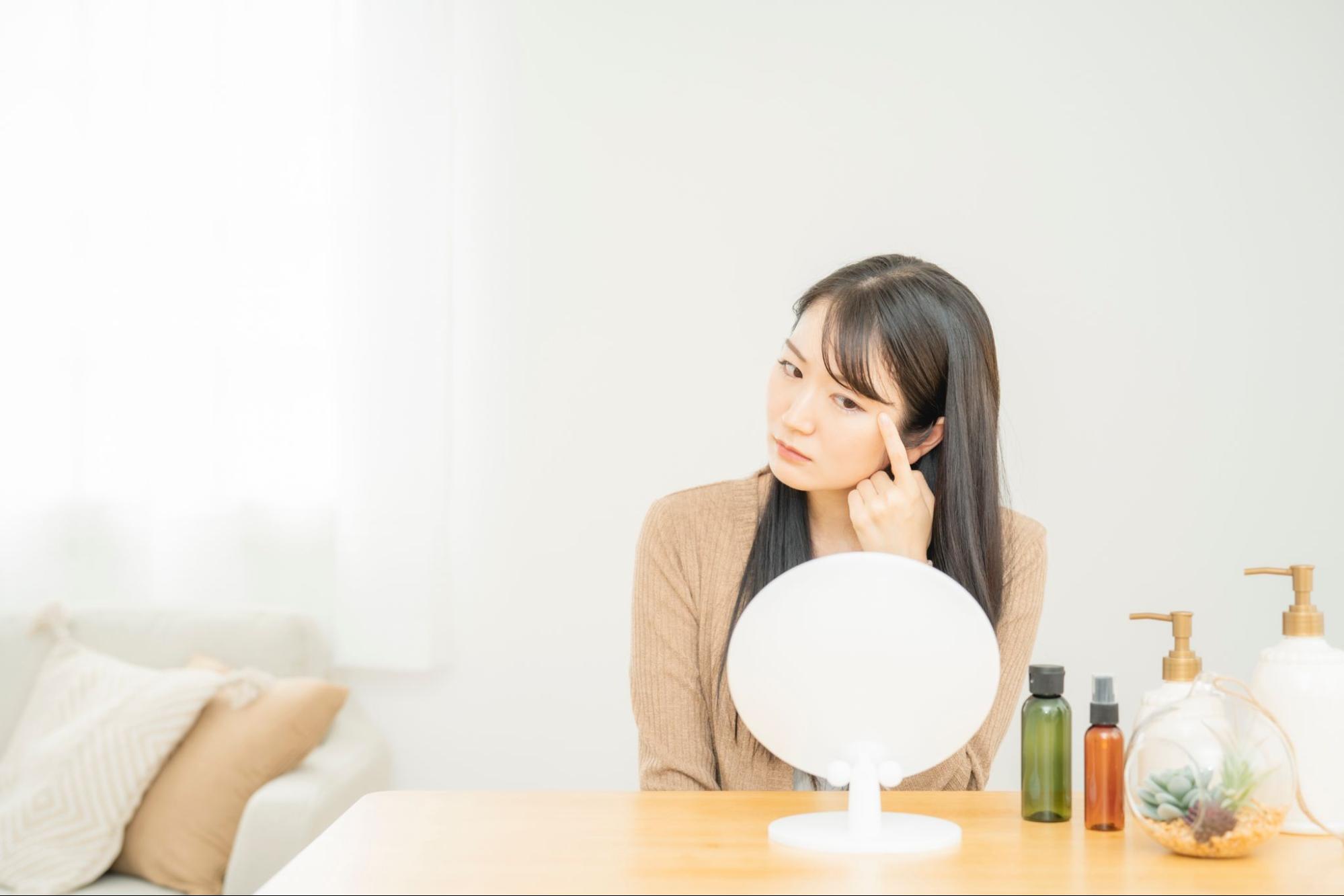 鏡を見て目元のたるみを気にしている女性