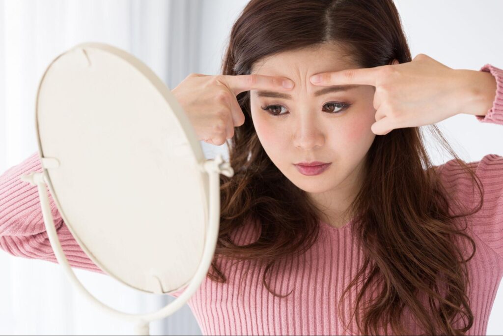 鏡を見ておでこや眉間付近に指を当てている女性