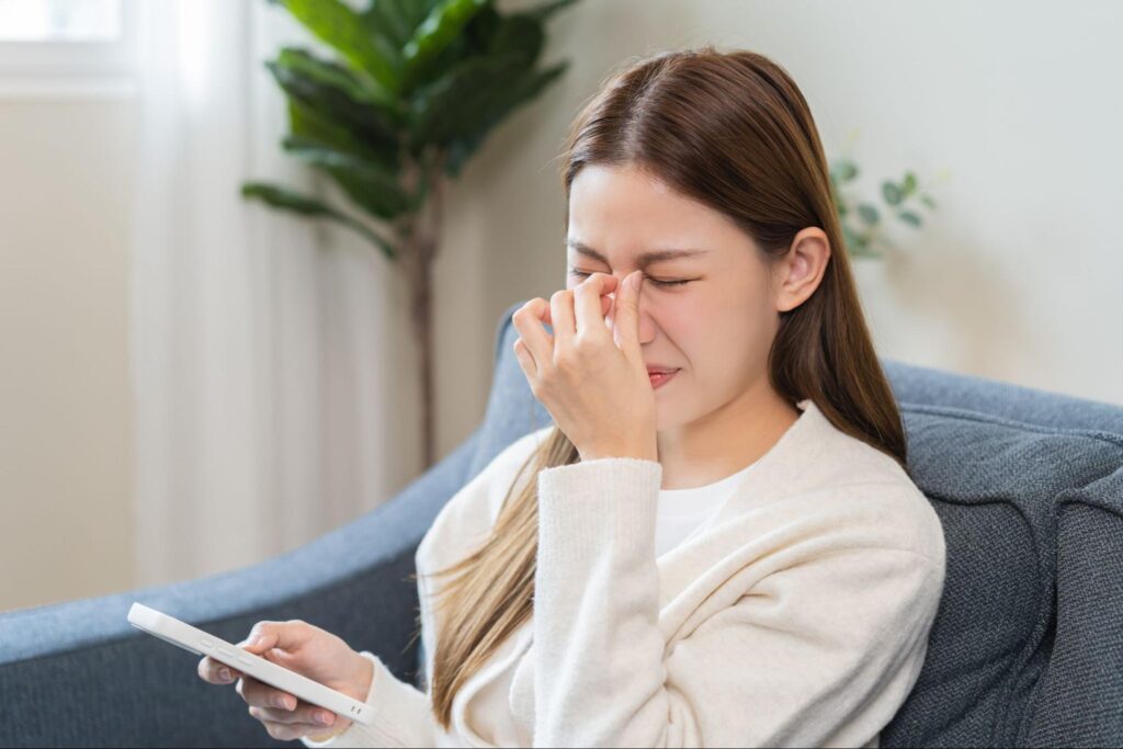 目を酷使したことで疲れ目になって目頭を押さえている女性